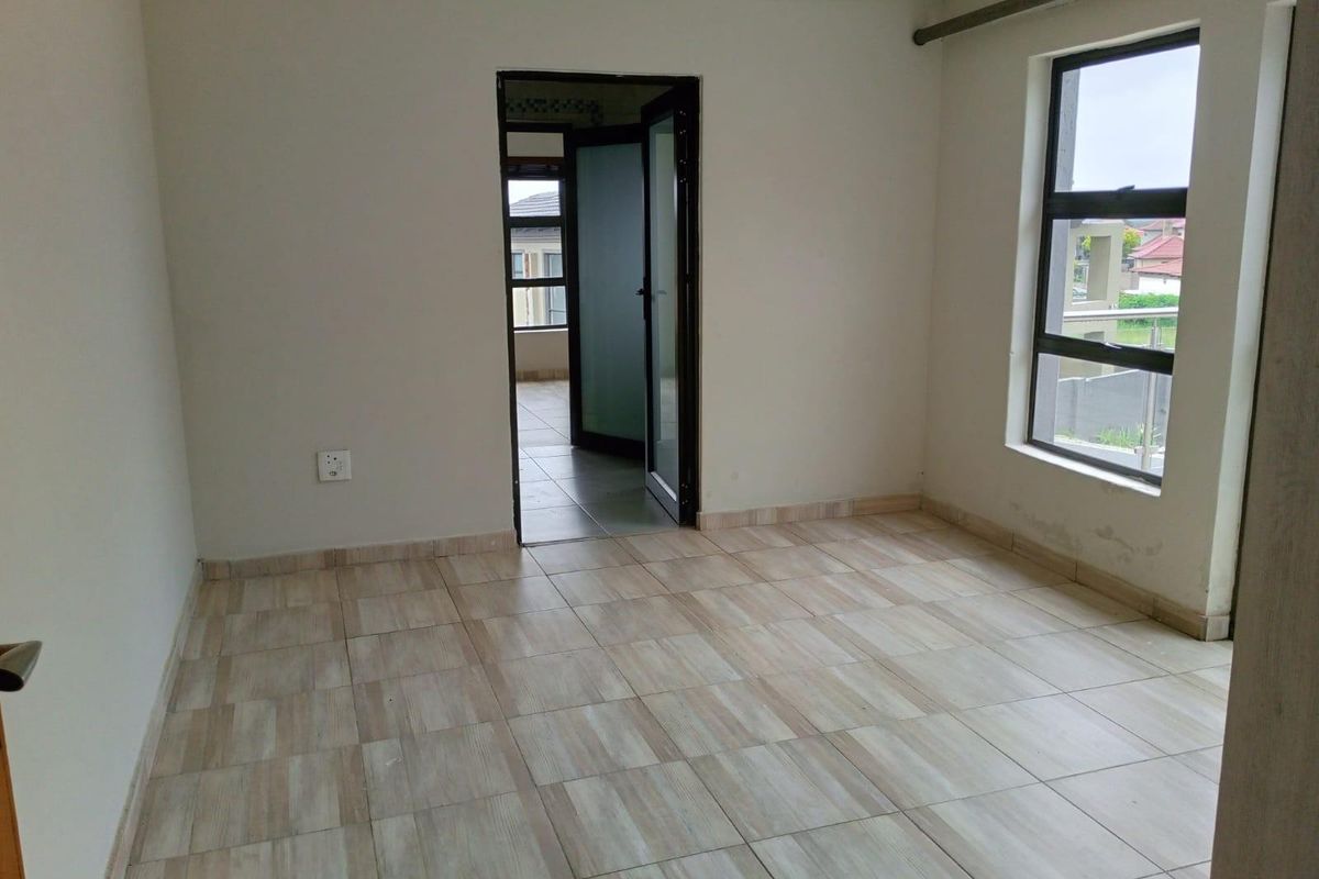 An empty bedroom featuring neutral tiled flooring, crown molding, and a large window providing natural light, with access to an adjacent room.