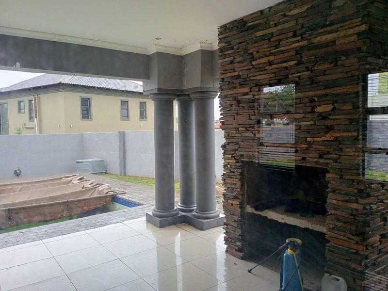 Covered patio area featuring a built-in stone fireplace, tiled flooring, and decorative columns, overlooking a swimming pool with a safety cover.