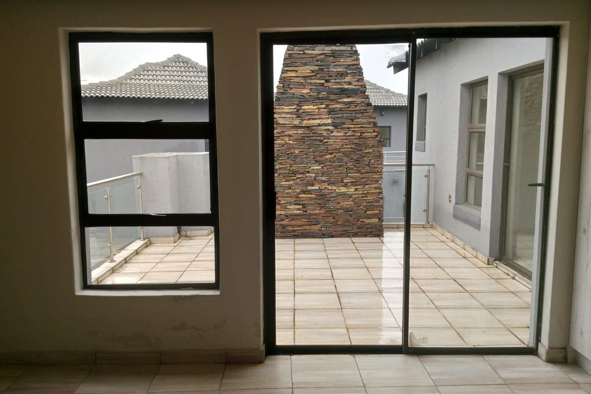 View from an interior space looking out onto a tiled balcony featuring a stone-clad outdoor fireplace and glass balustrades.