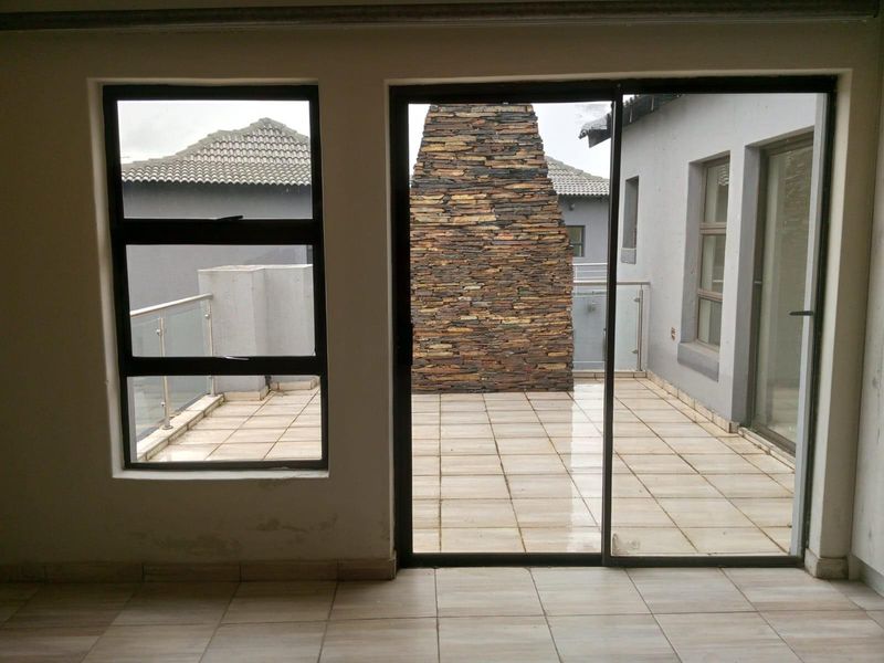 View from an interior space looking out onto a tiled balcony featuring a stone-clad outdoor fireplace and glass balustrades.