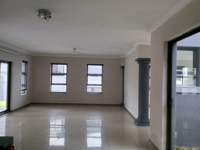 Spacious open-plan living area featuring large tiled flooring, decorative columns, and multiple windows providing natural light and access to the exterior.