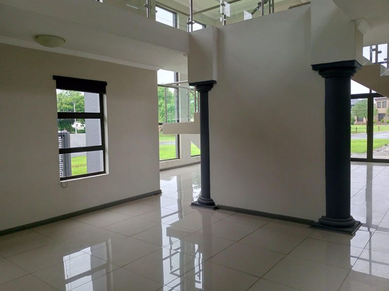 Spacious open-plan living area featuring polished floor tiles, decorative columns, and large windows providing ample natural light and garden views.