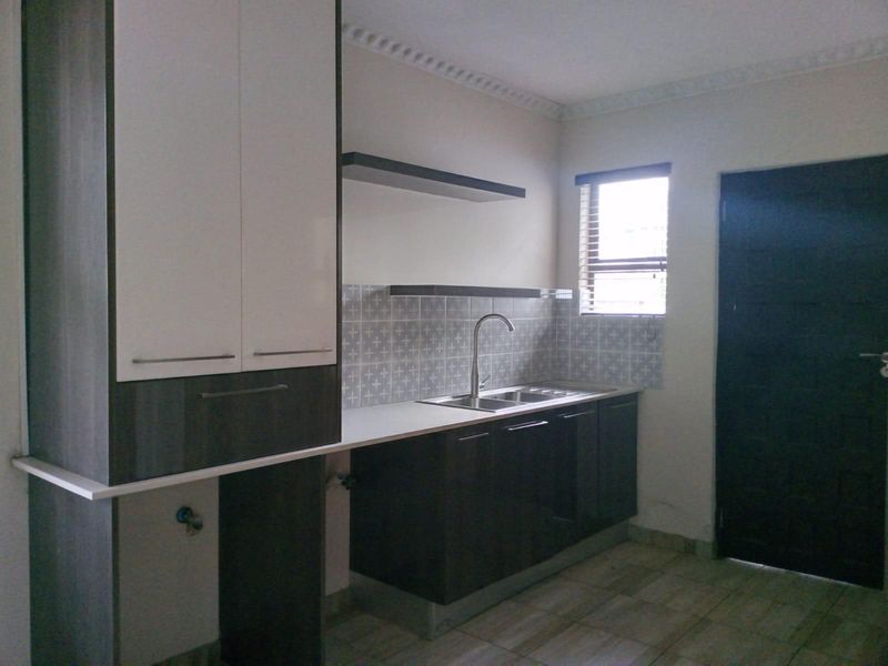 A modern kitchen featuring dark and white cabinetry, a stainless steel sink, tiled backsplash, and floating shelves.