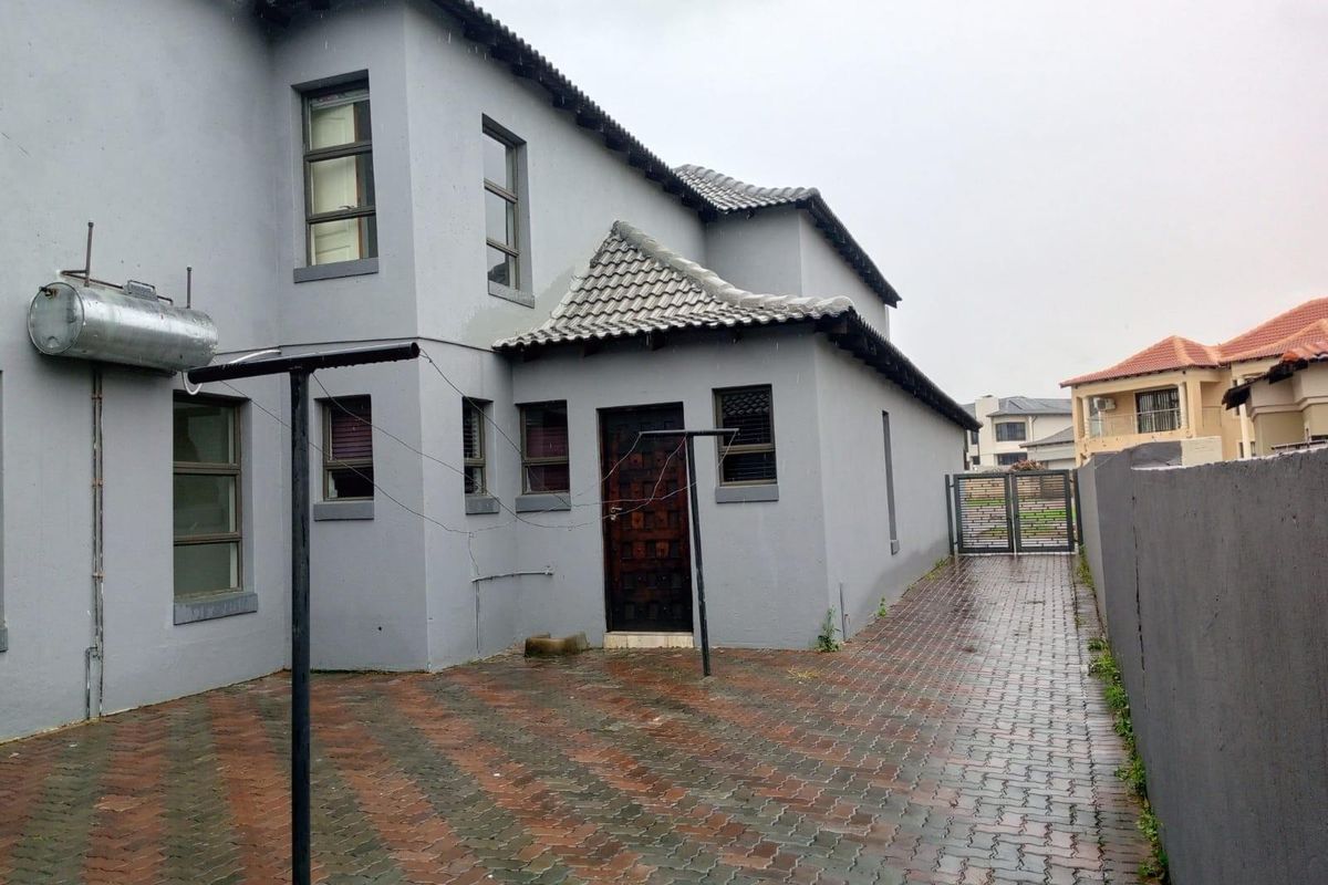 Rear exterior view of the double-story house featuring paved courtyard, external geyser, and secure gated side access.