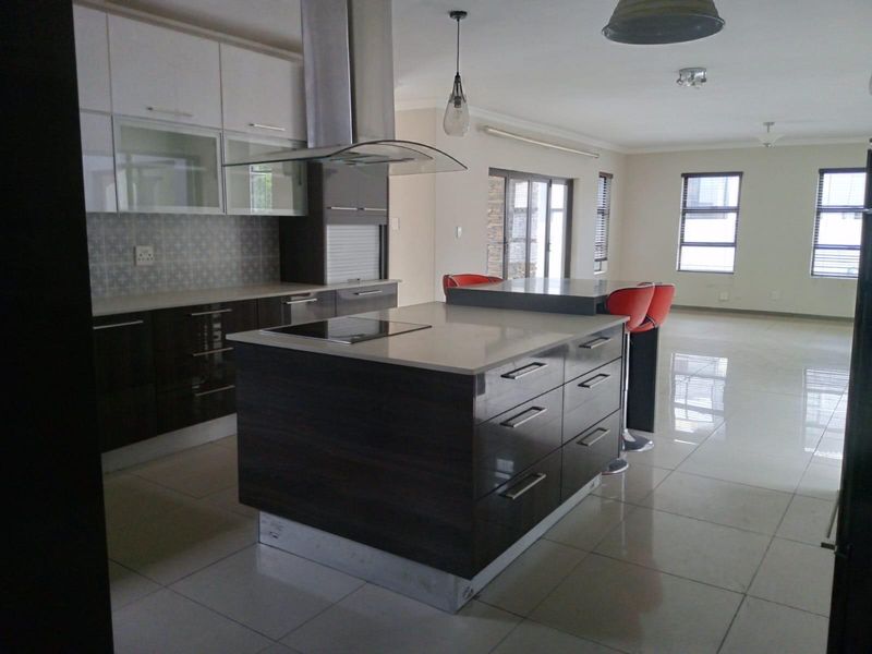 Modern open-plan kitchen featuring a central island with a built-in hob, sleek cabinetry, and tiled flooring, seamlessly flowing into the living area.