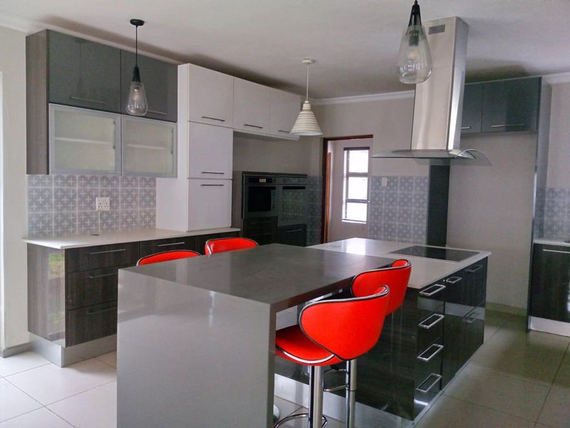 Modern kitchen featuring a central island with breakfast bar, built-in oven, sleek cabinetry, and a stainless steel extractor fan.