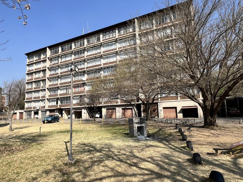 Exterior view of a multi-story townhouse complex featuring brick facade, large windows, and ground-level garage access with surrounding communal garden space.