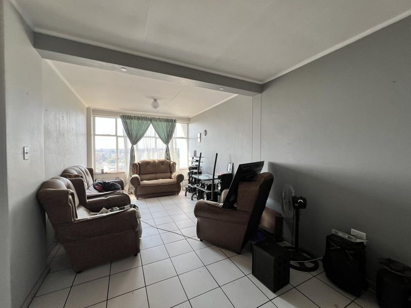 A spacious living room featuring large windows, neutral wall tones, and tiled flooring, offering a functional layout for comfortable daily living.