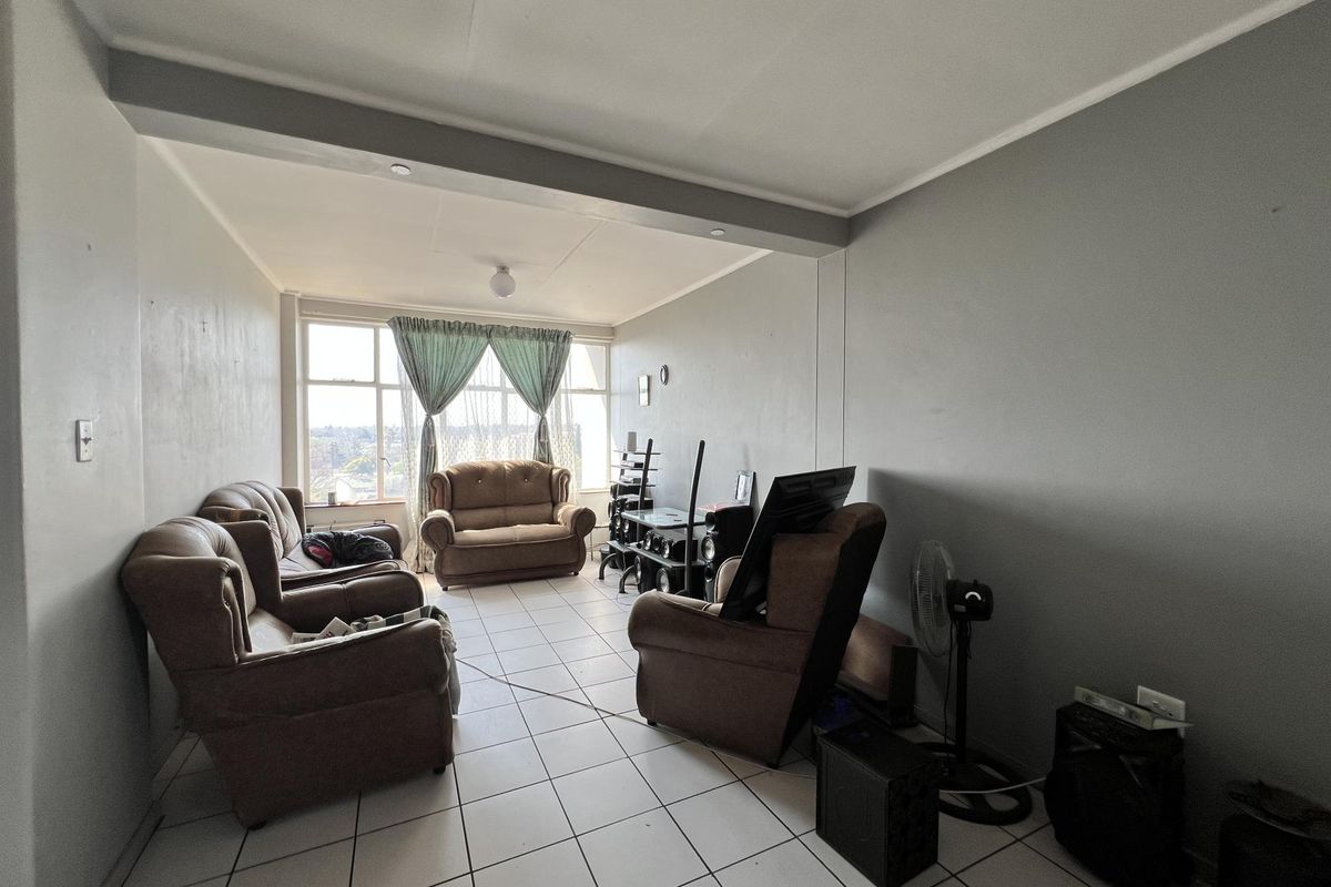A spacious living room featuring large windows, neutral wall tones, and tiled flooring, offering a functional layout for comfortable daily living.