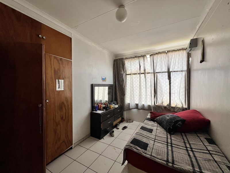 A bedroom featuring built-in wooden cupboards, tiled flooring, and large windows allowing natural light.