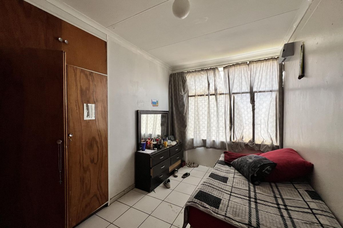 A bedroom featuring built-in wooden cupboards, tiled flooring, and large windows allowing natural light.