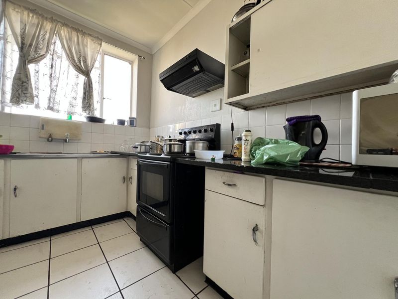 A functional kitchen featuring white cabinetry, tiled splashbacks, a black freestanding stove with extractor fan, and tiled flooring.