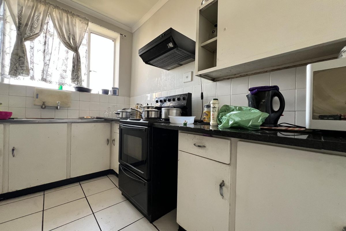 A functional kitchen featuring white cabinetry, tiled splashbacks, a black freestanding stove with extractor fan, and tiled flooring.