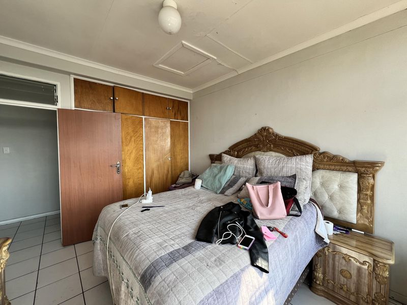 A bedroom featuring built-in wooden cupboards, tiled flooring, and a ceiling access hatch.