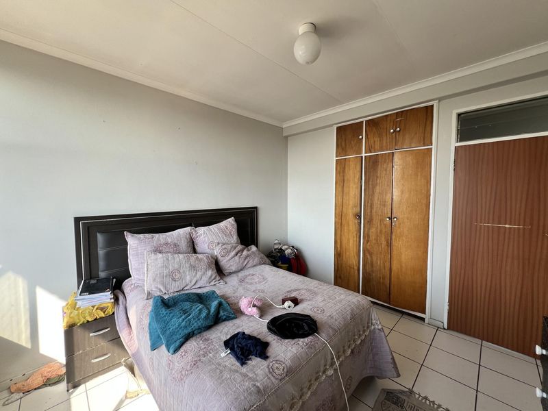 A bedroom featuring built-in wooden cupboards and tiled flooring, offering a functional space with neutral wall finishes.