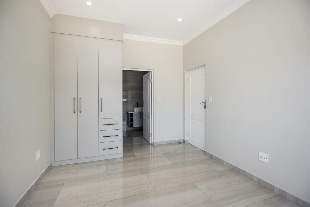 A bright, modern bedroom featuring neutral tiled flooring, built-in cabinetry, and direct access to an en-suite bathroom.