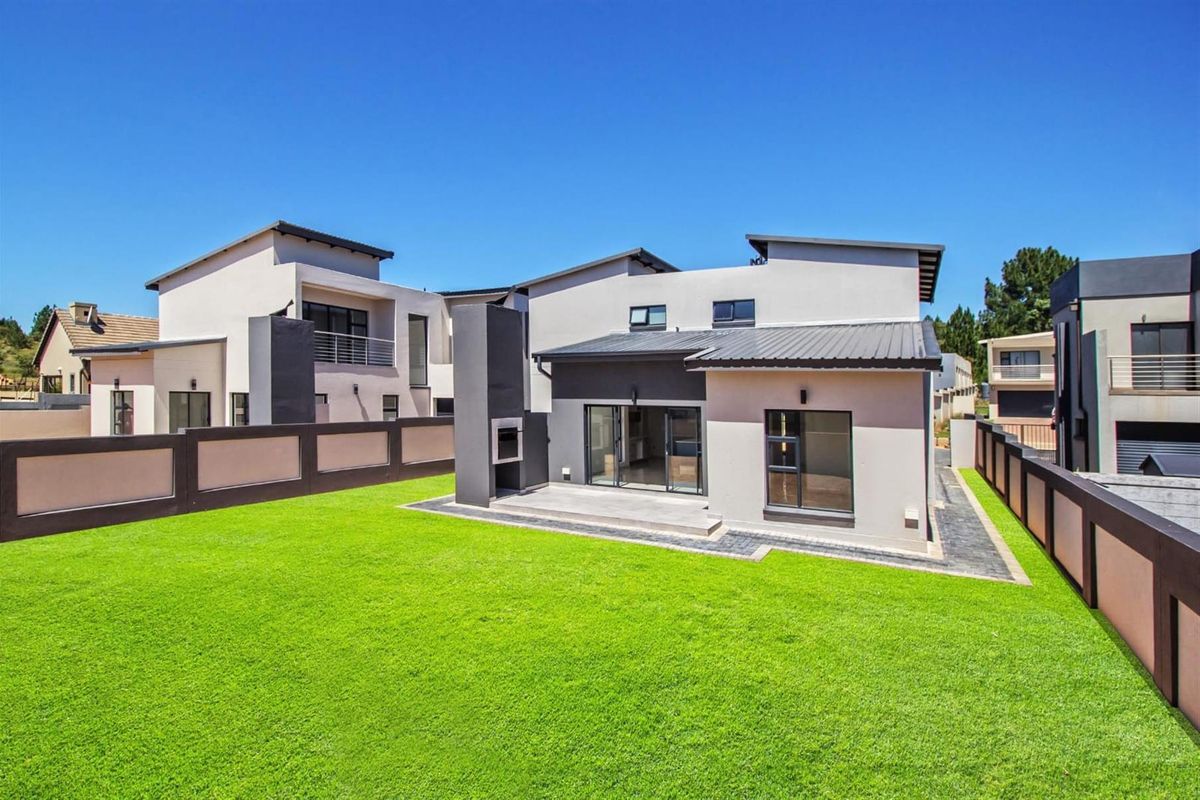 A modern rear exterior view of the house featuring a manicured lawn, a paved patio area, and a built-in outdoor fireplace.