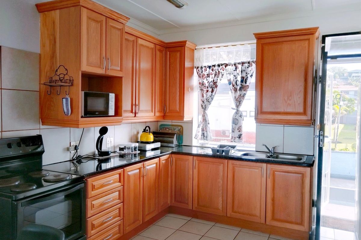 A functional kitchen featuring wooden cabinetry, dark granite countertops, a built-in stove, and a double sink, with direct access to an outdoor area.