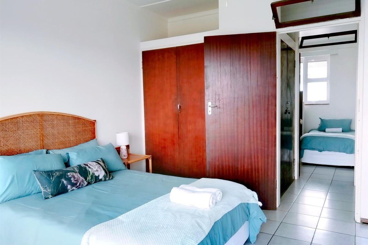 A bedroom featuring built-in wooden cupboards and tiled flooring, with an adjacent room visible through the doorway.