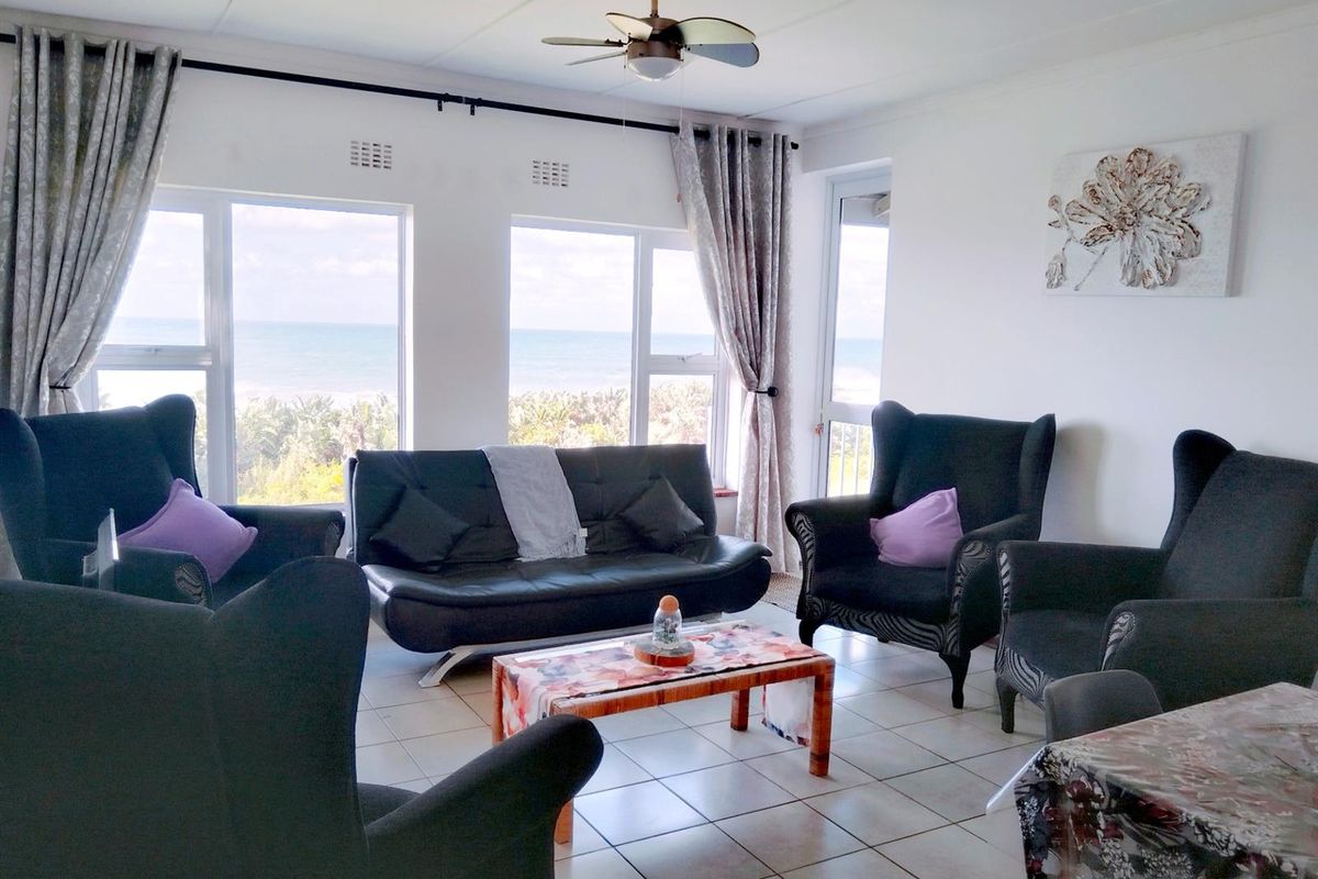 Bright living area featuring large windows with ocean views, tiled flooring, and a ceiling fan, offering a comfortable space for relaxation.
