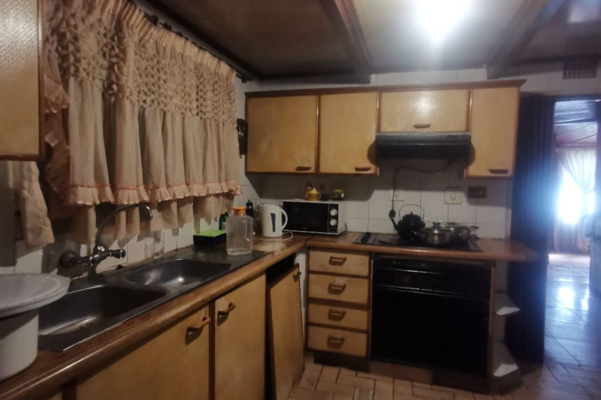 A dated kitchen featuring wooden cabinetry, a built-in oven with extractor fan, double sink, and herringbone-patterned tiled flooring.