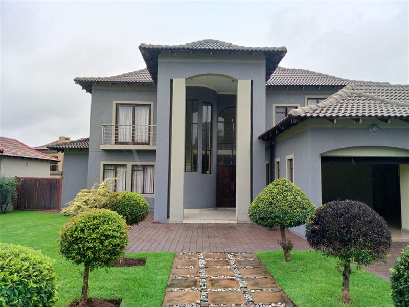 A well-maintained double-story residence featuring a grand entrance, tiled roof, paved walkway, and manicured garden.