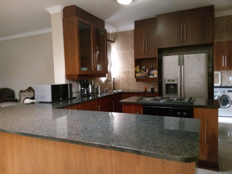 A functional kitchen featuring dark wood cabinetry, granite countertops, a breakfast bar, and integrated appliances including a hob and oven.