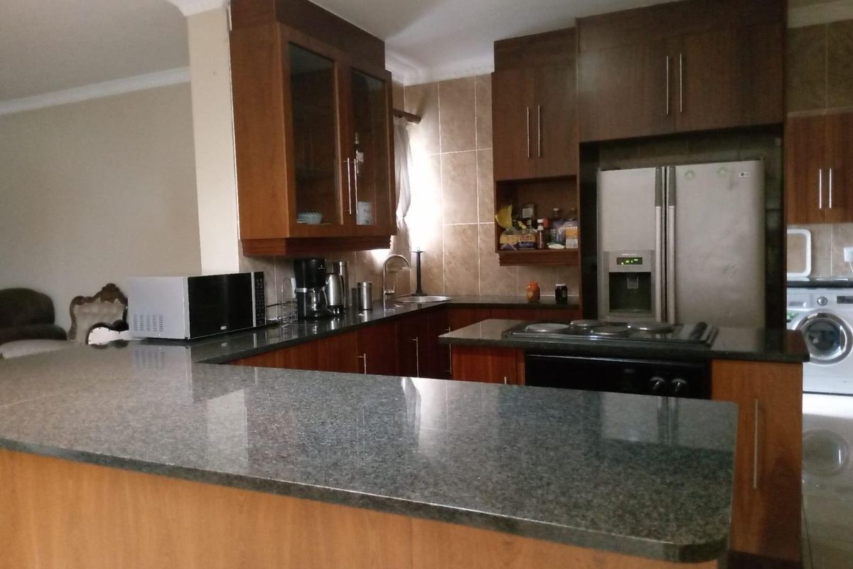 A functional kitchen featuring dark wood cabinetry, granite countertops, a breakfast bar, and integrated appliances including a hob and oven.