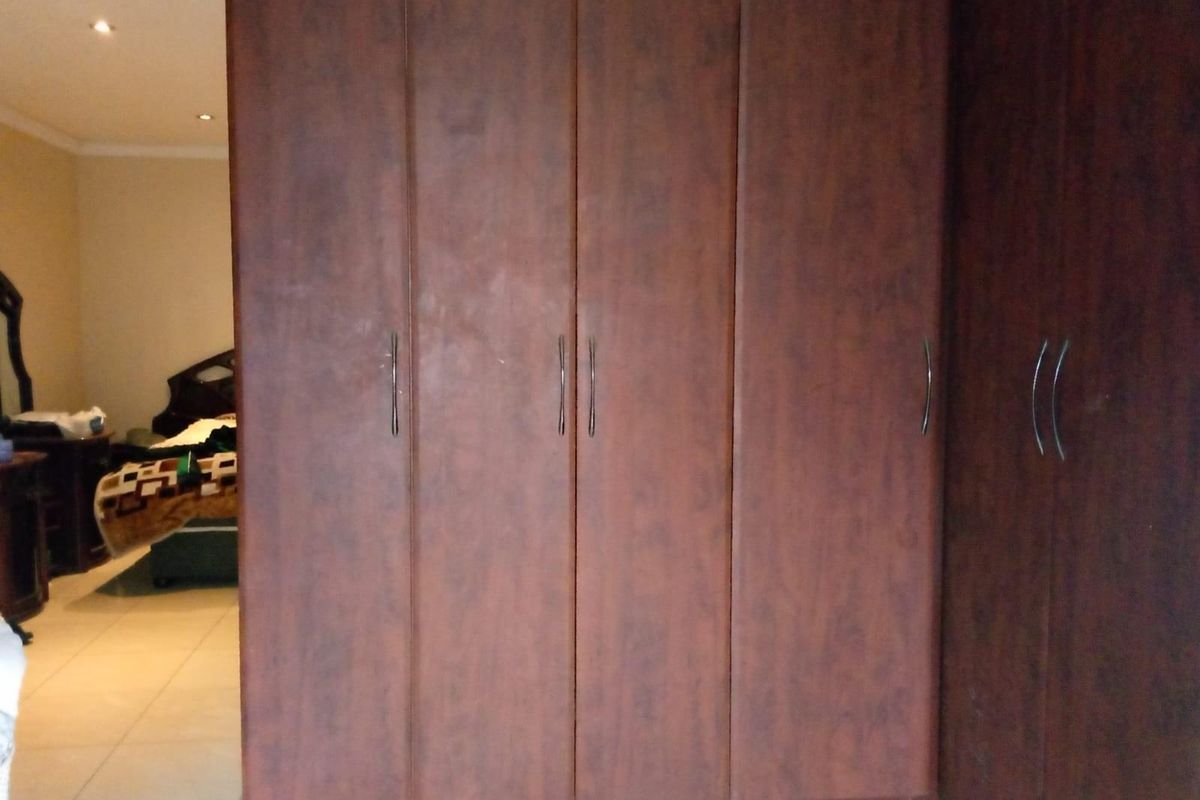 A bedroom featuring built-in floor-to-ceiling wooden wardrobes with modern handles, providing ample storage space.