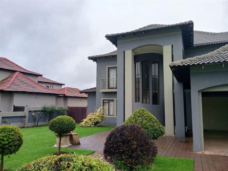 A modern double-story residential facade featuring a prominent arched window, tiled roof, and a paved walkway leading to the entrance.