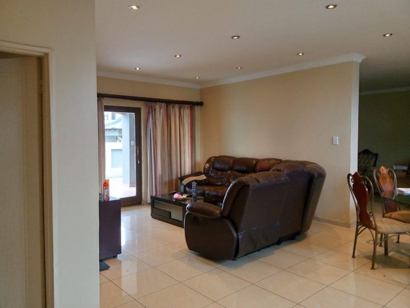 Spacious open-plan living area featuring neutral tiled flooring, recessed downlighting, and direct access to an outdoor patio through a glass door.