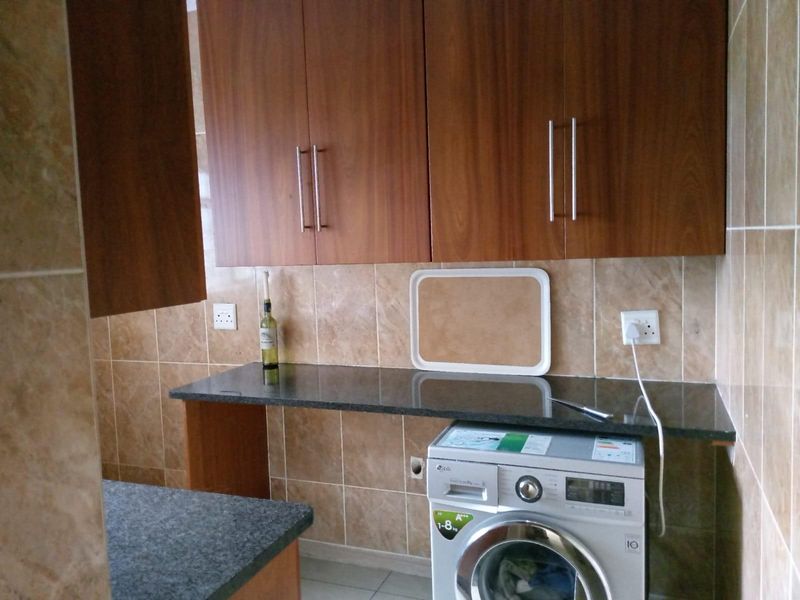 A functional laundry area featuring dark wood cabinetry, granite countertops, and tiled walls with space for a front-loading washing machine.