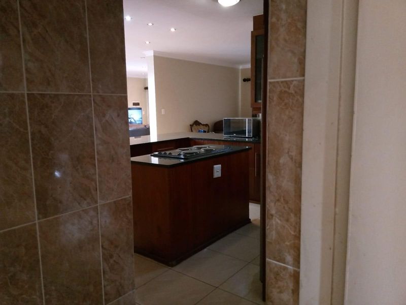 A view into a kitchen featuring a central island with a built-in hob, dark wood cabinetry, and tiled flooring, leading into an open-plan living area.