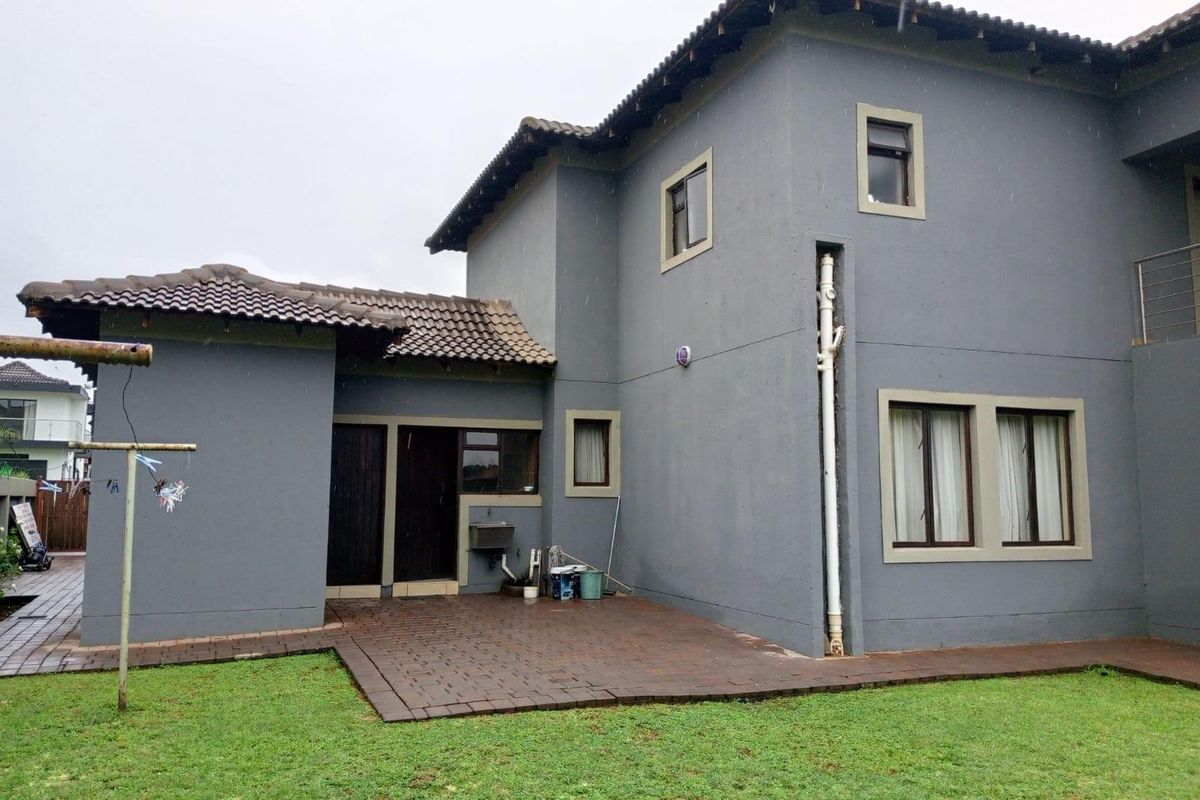 Rear view of the two-story house featuring a paved patio area, tiled roof, and grey exterior walls with a small garden.