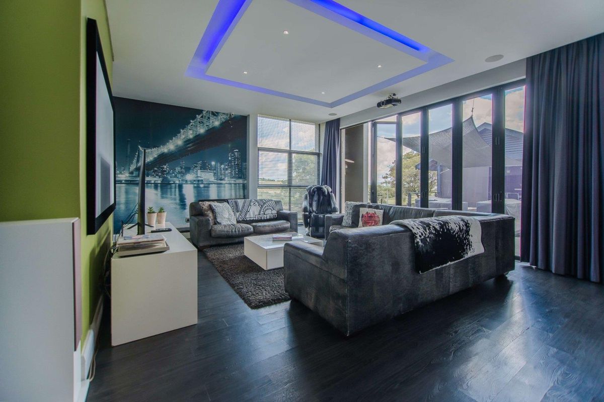 Modern living room featuring dark hardwood flooring, recessed tray ceiling with integrated blue LED lighting, and large floor-to-ceiling glass sliding doors.