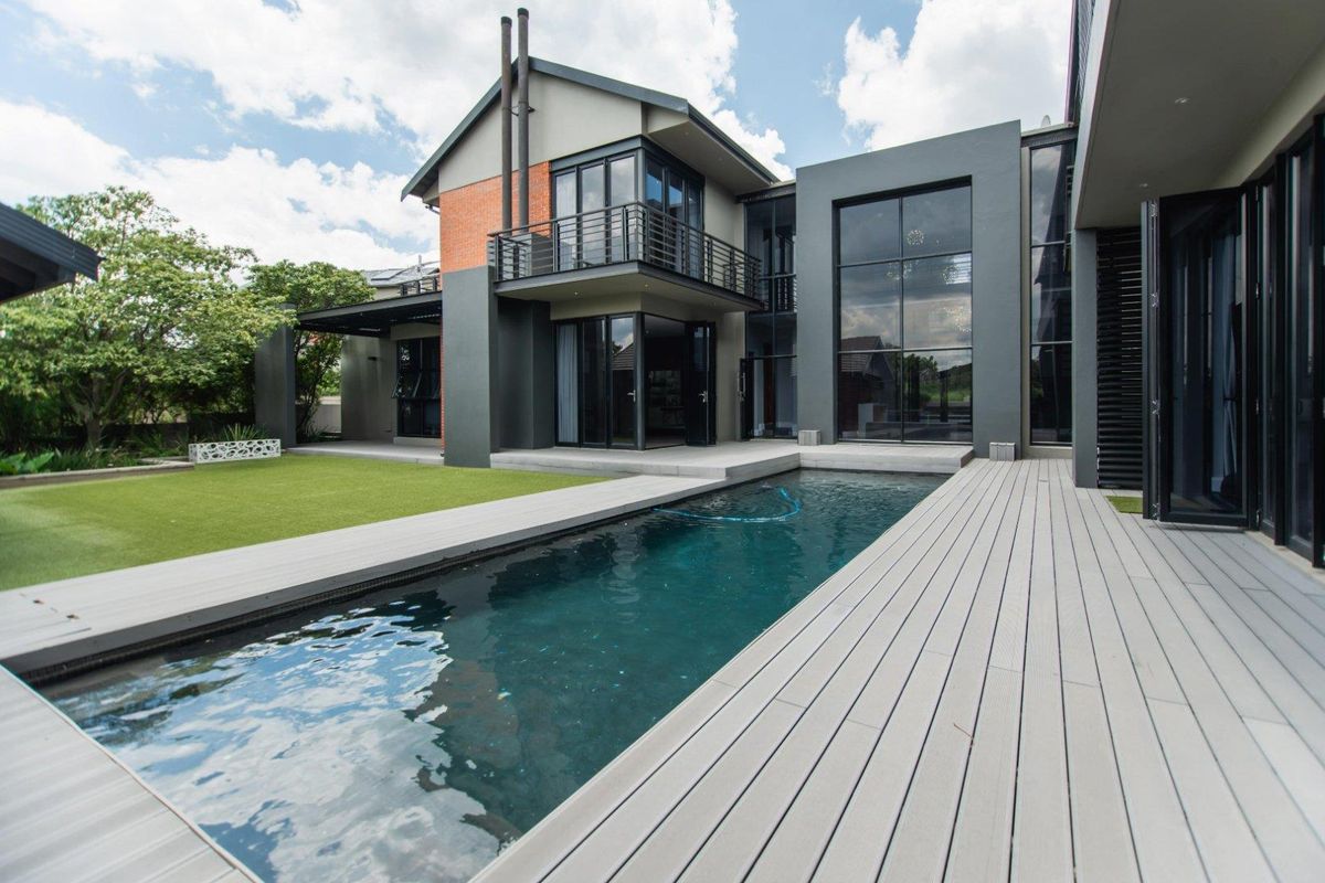 Modern double-story residence featuring a swimming pool, composite decking, and expansive glass facades opening onto a landscaped garden area.