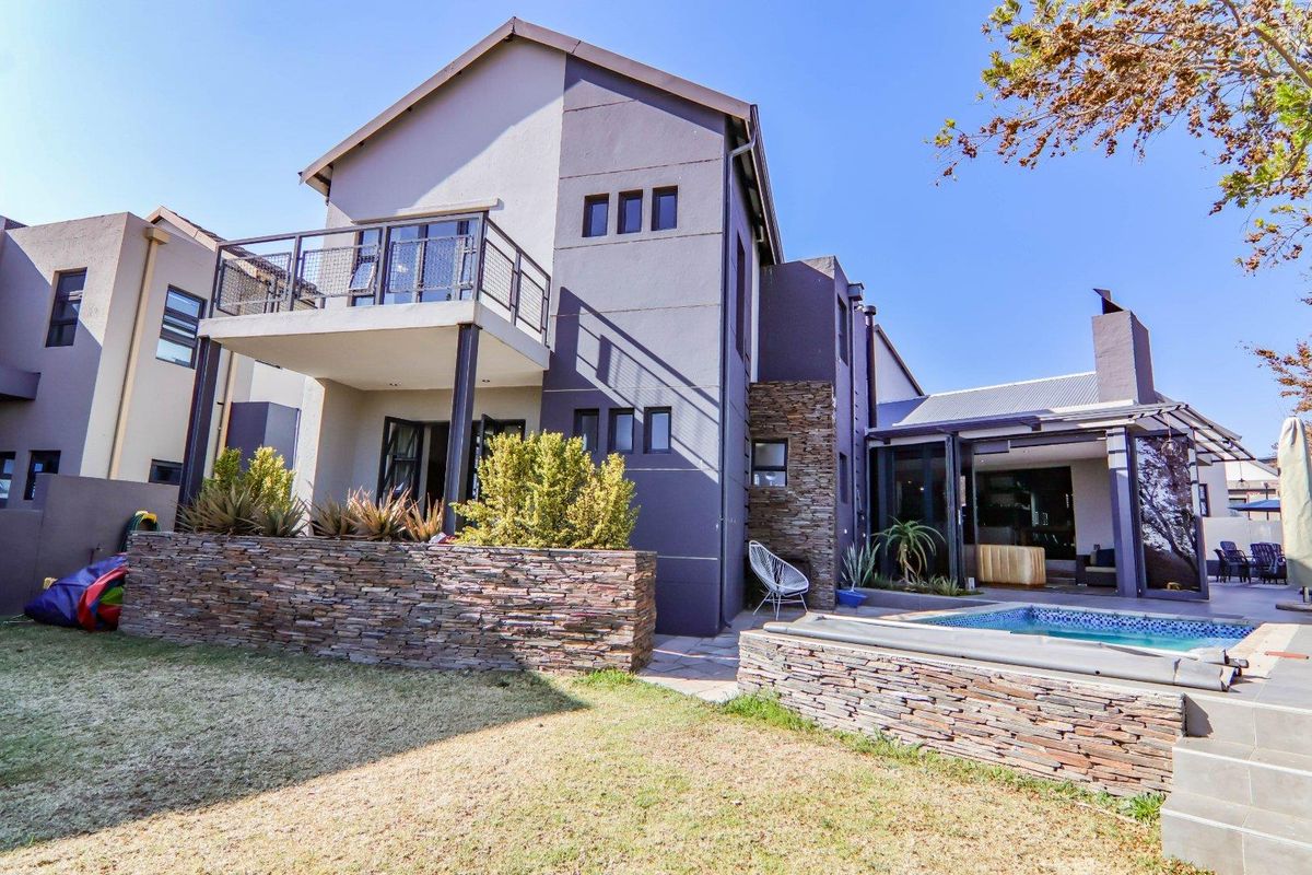 Rear view of a modern two-story house featuring a swimming pool, stone-clad retaining walls, a balcony, and a covered patio area.