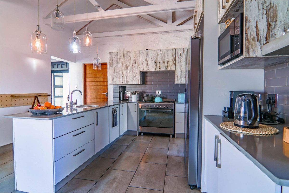Modern kitchen featuring stone countertops, subway tile backsplash, built-in oven with extractor fan, and exposed timber ceiling beams.