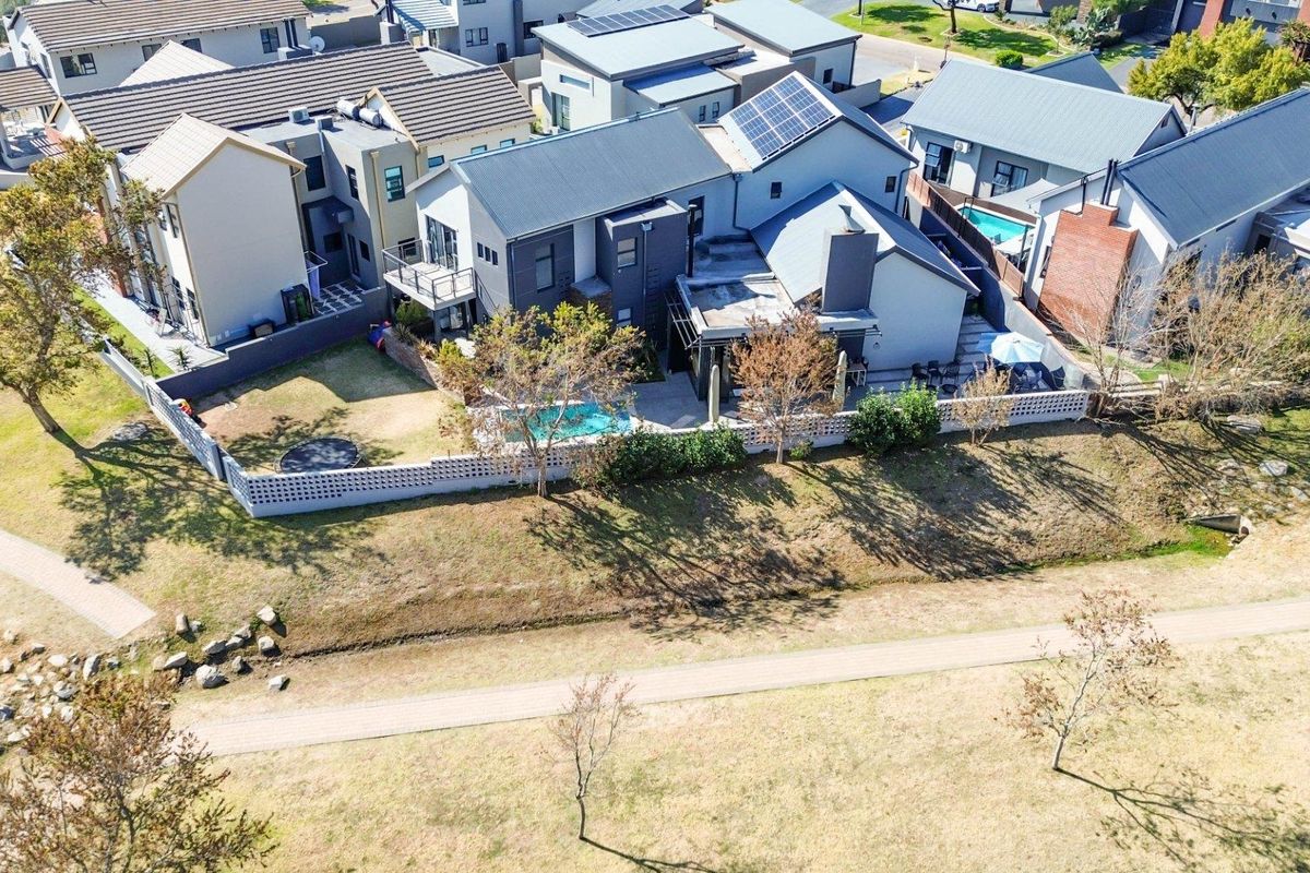 Aerial view of a modern residential property featuring a swimming pool, landscaped garden, and solar panels on the roof.