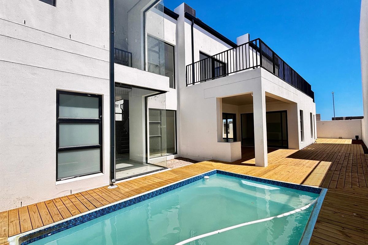Modern rear exterior featuring a swimming pool, timber decking, a covered patio area, and a balcony with metal railings.