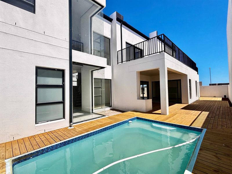 Modern rear exterior featuring a swimming pool, timber decking, a covered patio area, and a balcony with metal railings.