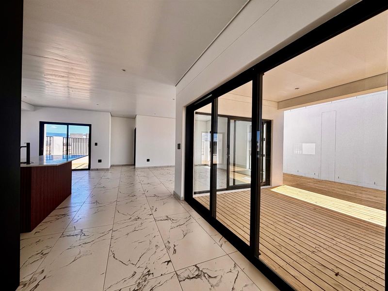 Spacious open-plan living area featuring modern marble-look floor tiles, large sliding glass doors, and seamless access to an outdoor wooden deck.