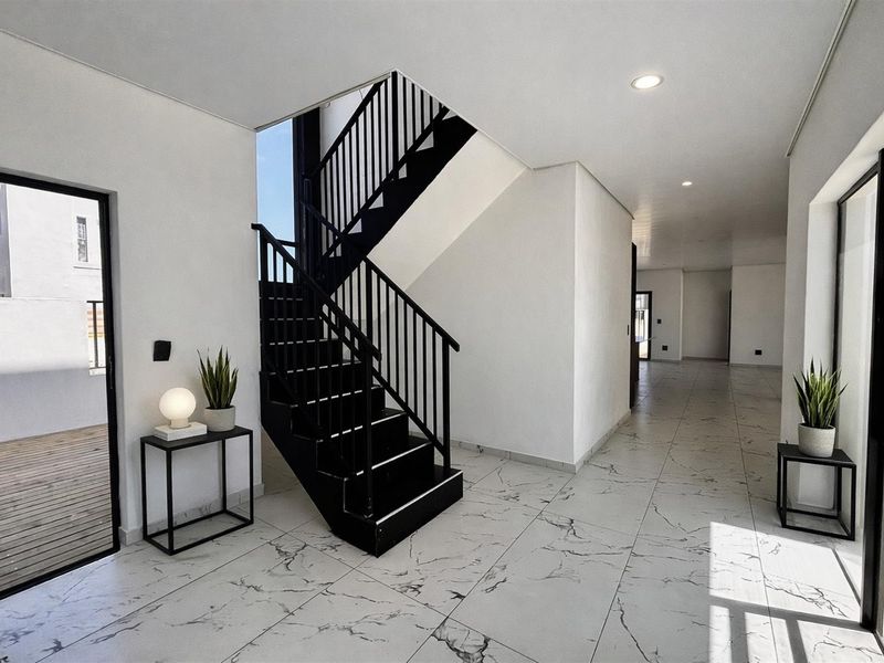 Spacious modern entrance hall featuring a striking black staircase, marble-look tiled flooring, and large glass doors leading to an outdoor deck area.