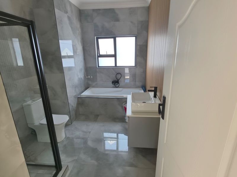 Modern bathroom featuring a glass-enclosed shower, a built-in bathtub, a vessel sink vanity, and contemporary grey floor-to-ceiling tiling with wood-look accent paneling.
