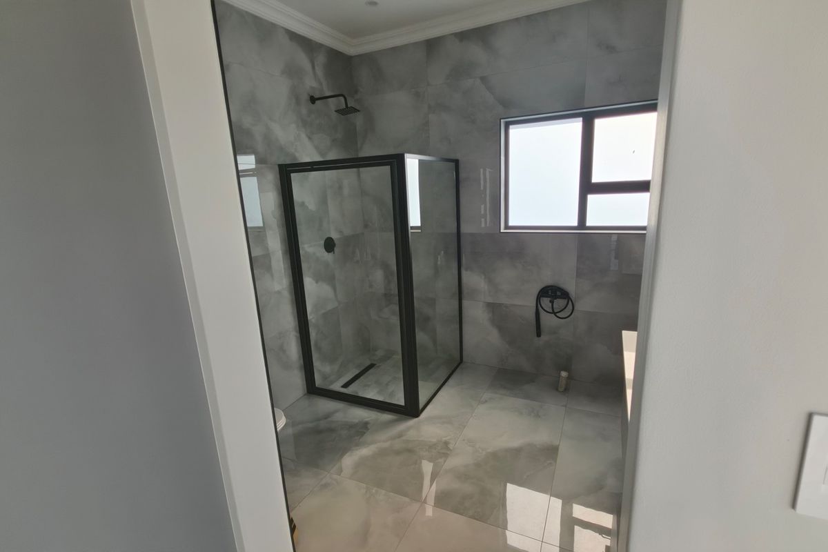 Modern bathroom featuring a walk-in shower with a black frame, contemporary grey marble-look tiling, and clean, minimalist finishes.