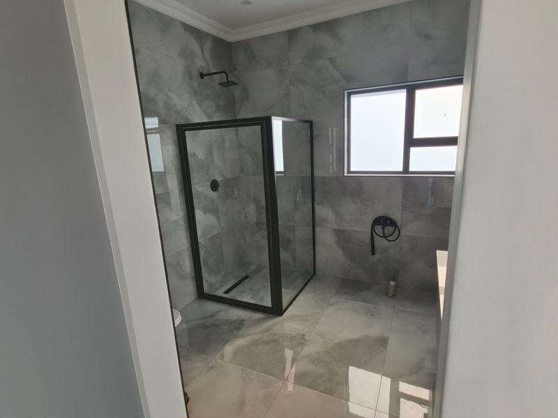 Modern bathroom featuring a walk-in shower with a black frame, contemporary grey marble-look tiling, and clean, minimalist finishes.