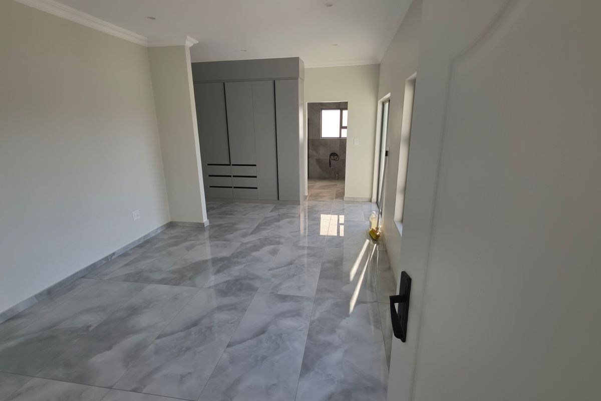 A modern, empty bedroom featuring polished grey marble-look floor tiles, built-in cupboards, and neutral wall finishes with access to an en-suite bathroom.