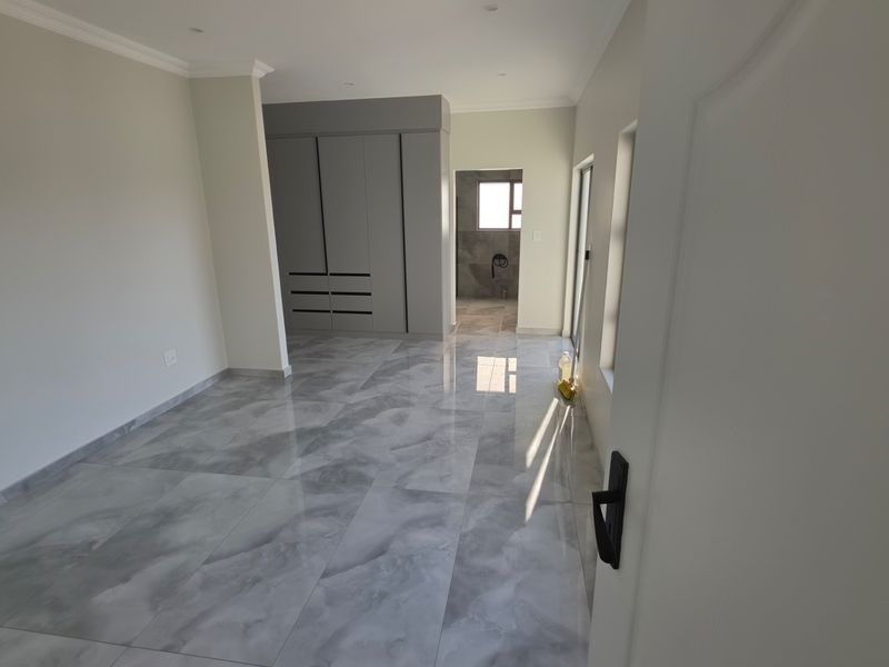 A modern, empty bedroom featuring polished grey marble-look floor tiles, built-in cupboards, and neutral wall finishes with access to an en-suite bathroom.