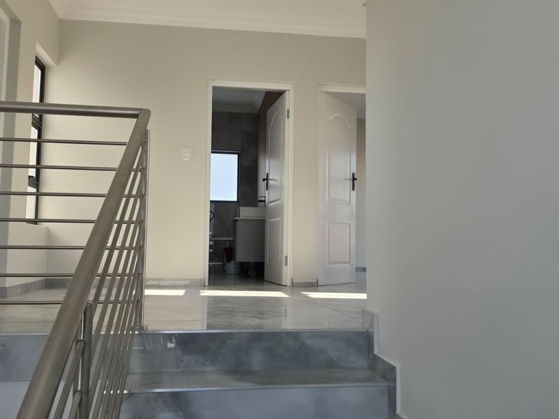 A bright, modern hallway landing featuring tiled flooring, a stainless steel balustrade, and access to adjacent rooms.