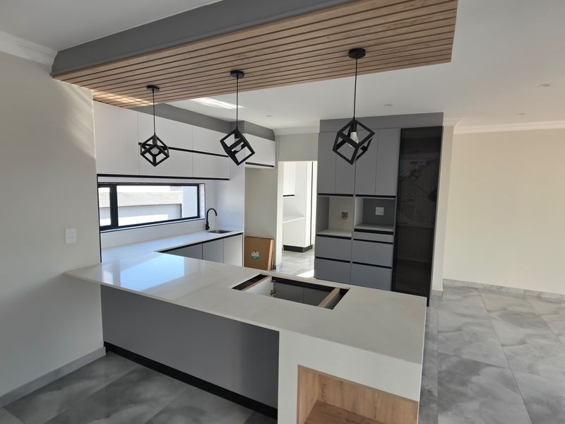 Modern kitchen featuring sleek cabinetry, a central island with quartz countertops, and stylish pendant lighting, awaiting final appliance installation.